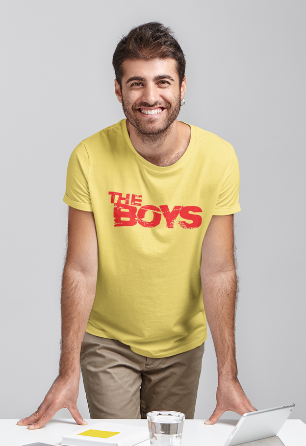 A young man standing wearing a yellow Tshirt with 'The Boys' printed on it.